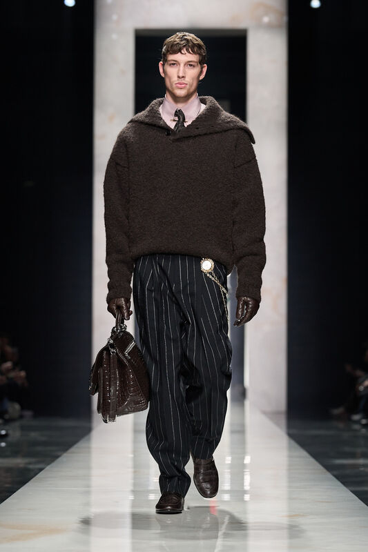 Модель в тёмно-коричневом свитере и полосатых брюках, дополненных стильной сумкой, создаёт атмосферу современного шика