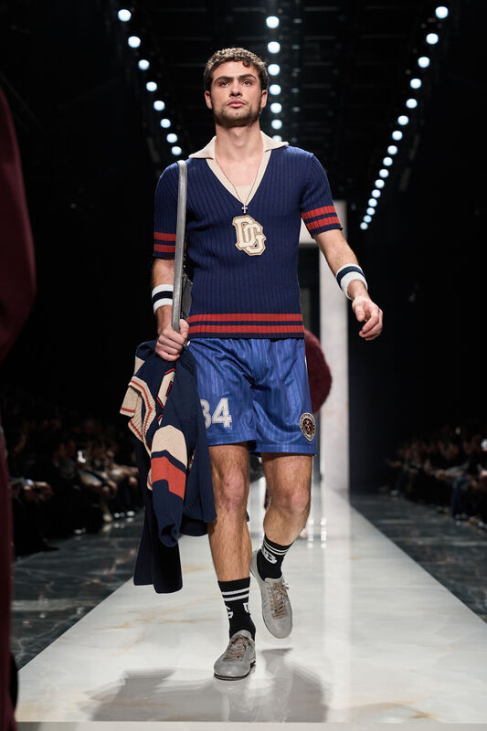 Спортивный образ с синей вязаной футболкой и шортами, дополненный стильным свитером на плечах и крупной подвеской