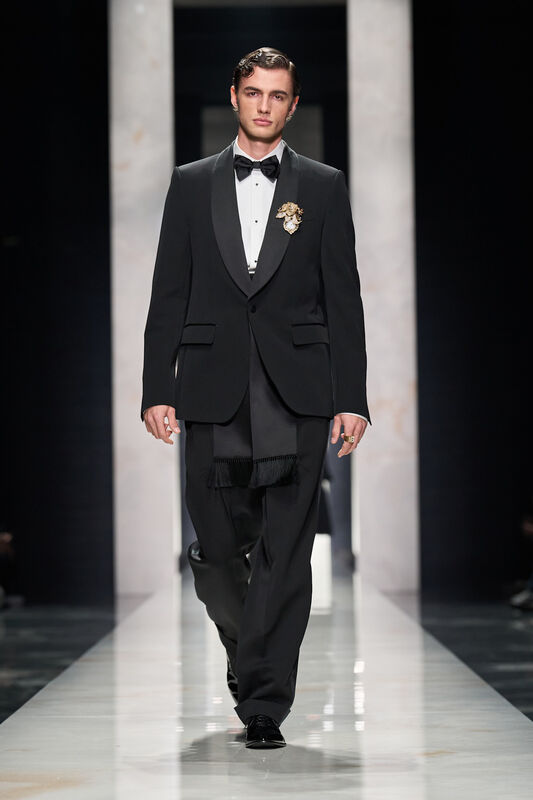 Классический черный смокинг с бабочкой и изысканной брошей, создающий атмосферу утонченности на подиуме