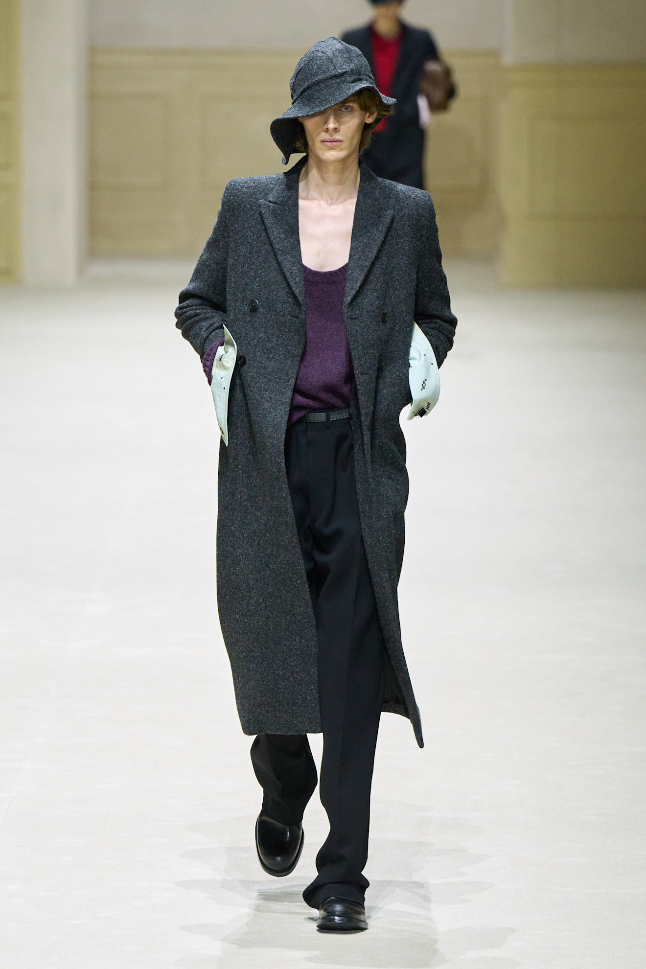 Модель в сером пальто с широкими лацканами и шляпе, подчеркивающей стильный образ, сочетает с темными брюками