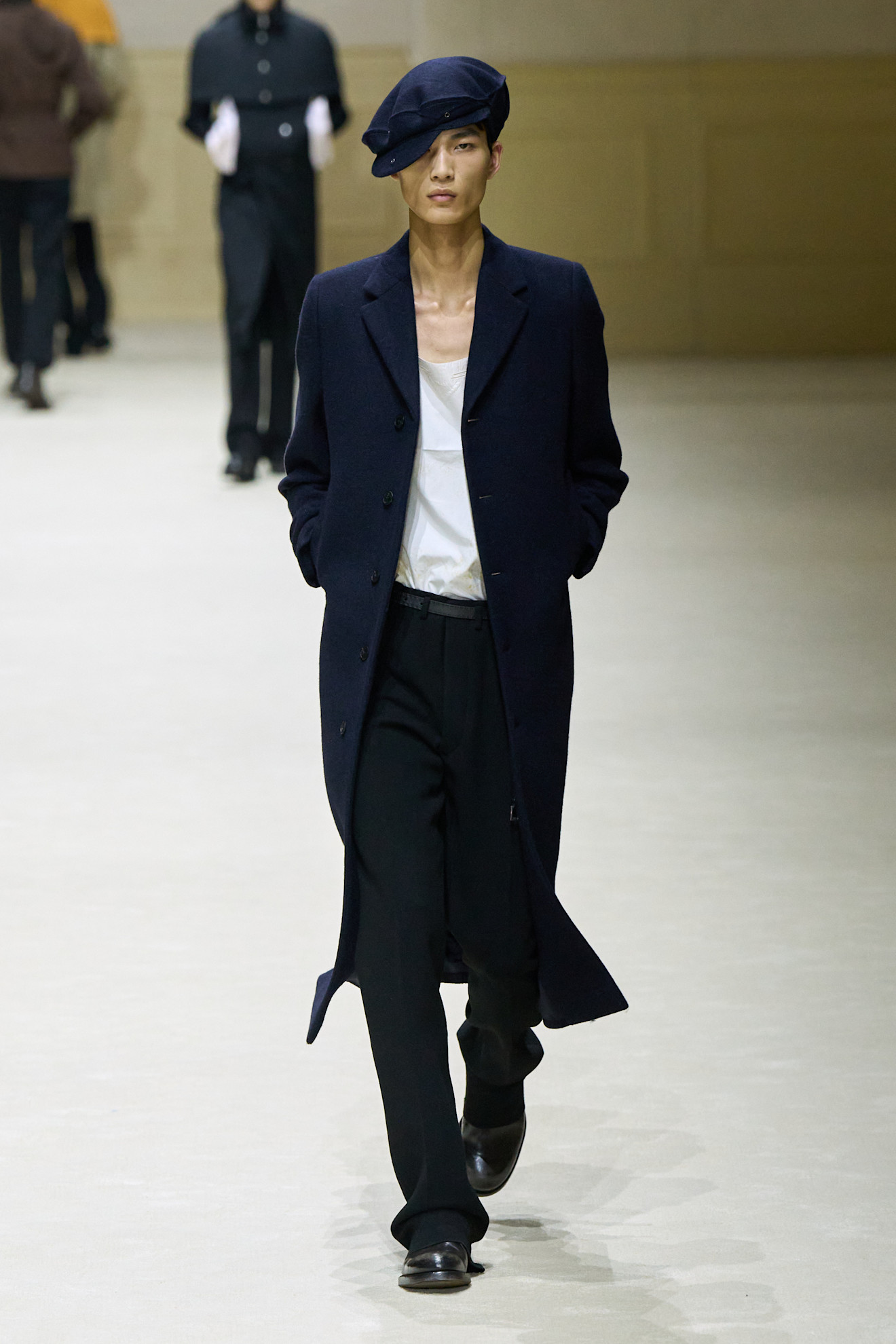 Модель в темно-синем пальто и черных брюках, с беретом на голове, излучает уверенность и стиль в каждом шаге