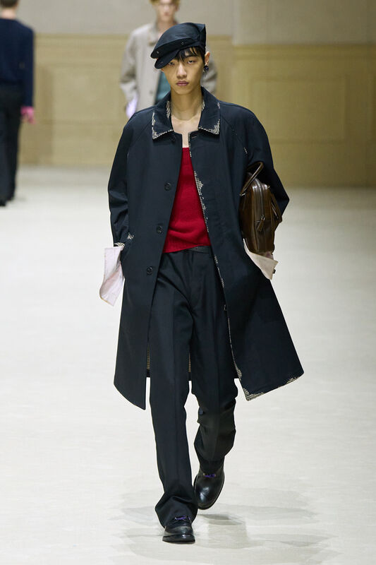 Модель в черном пальто с текстурированными деталями и красным свитером, элегантно несущая коричневую сумку