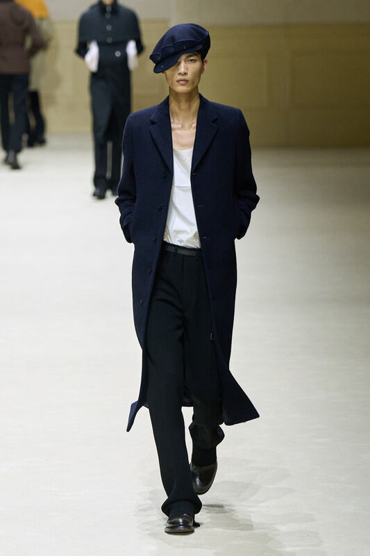 Модель в темно-синем пальто и черных брюках, с беретом на голове, излучает уверенность и стиль в каждом шаге