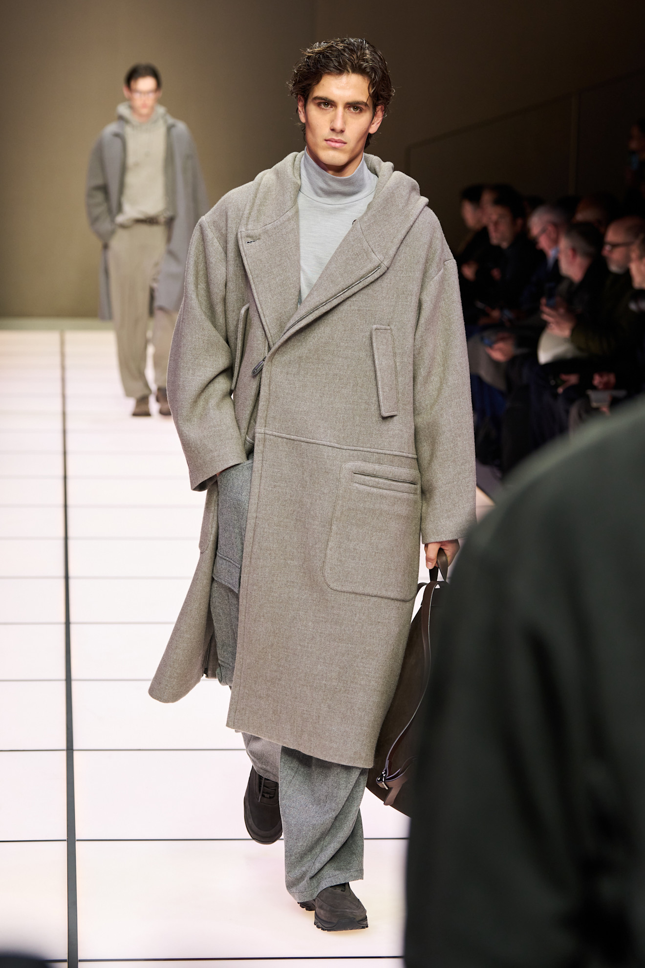 Модель в объемном сером пальто с капюшоном и светлом свитере, создающая уютный и современный образ