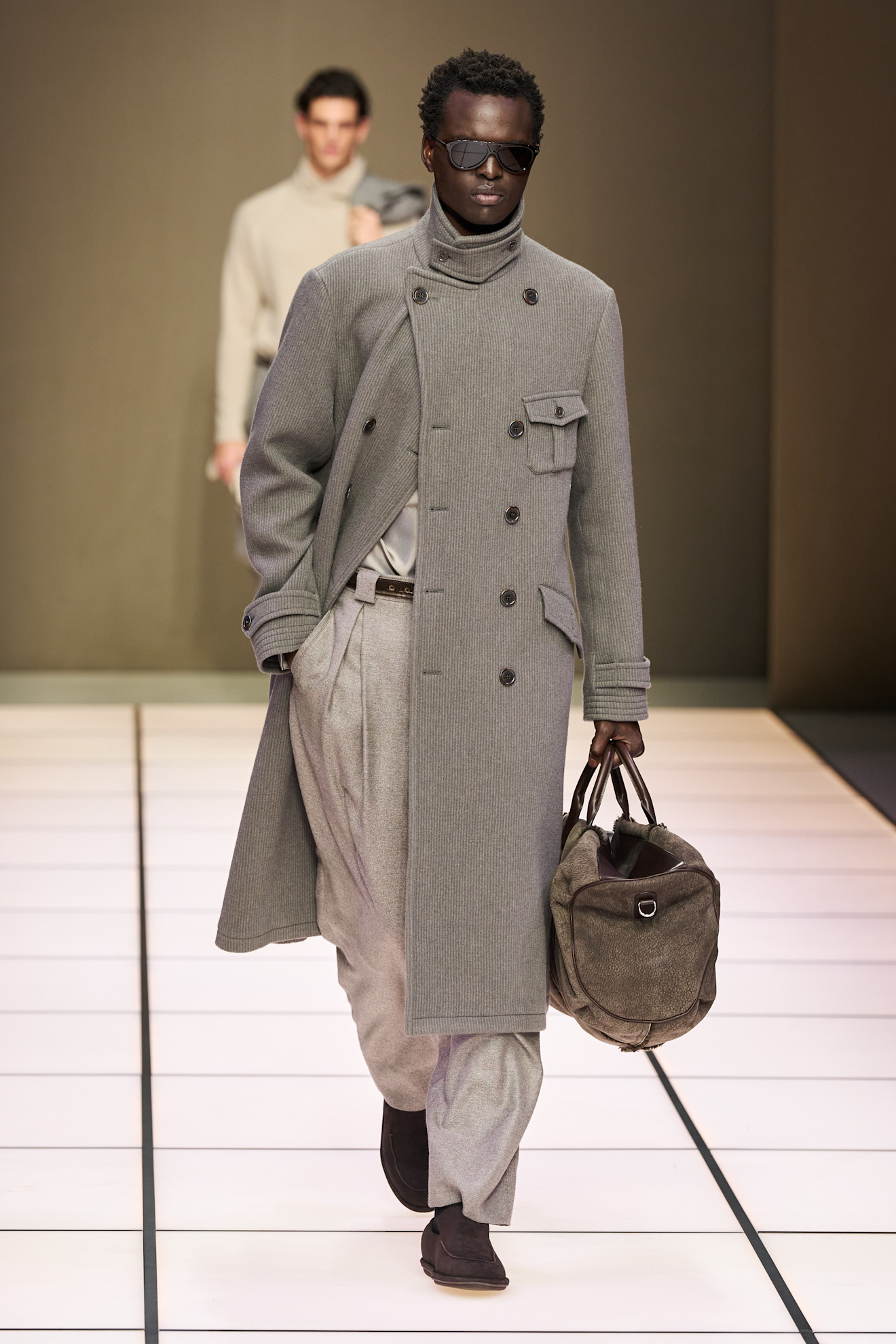 Модель в сером пальто с текстурой, сочетает элегантность и комфорт, дополняя образ стильной сумкой и солнцезащитными очками