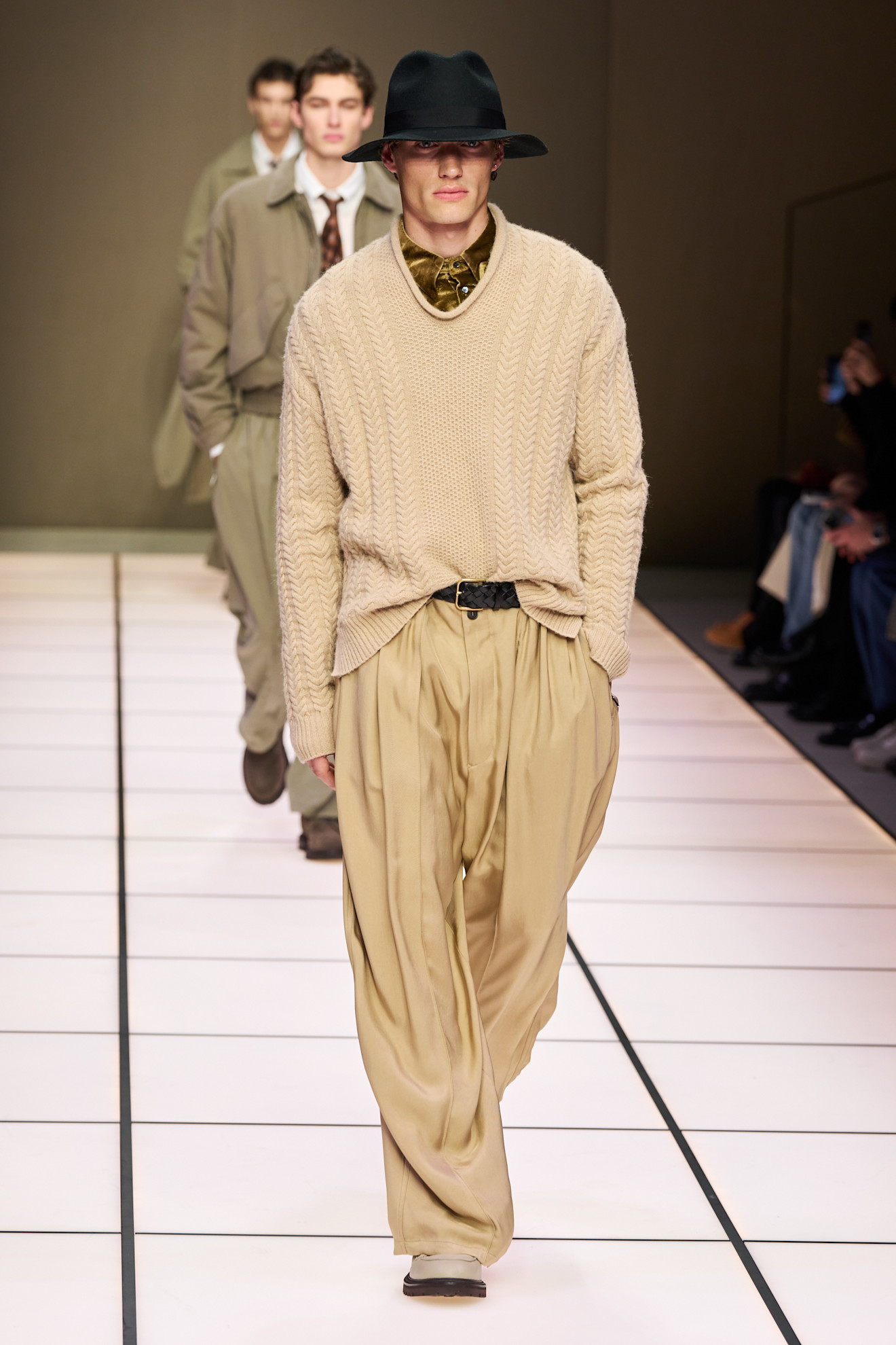 Модель в бежевом свитере и брюках, дополненная черной шляпой, создает атмосферу непринужденной элегантности