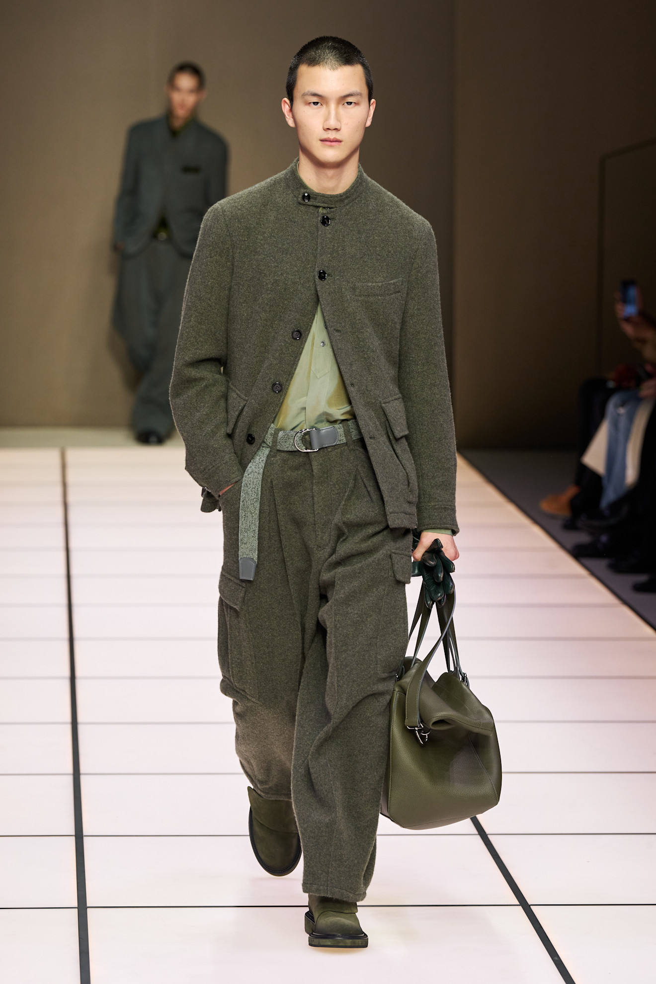 Модель в уютном оливковом костюме из шерсти с карманами, дополняет образ стильной сумкой и ботинками в тон