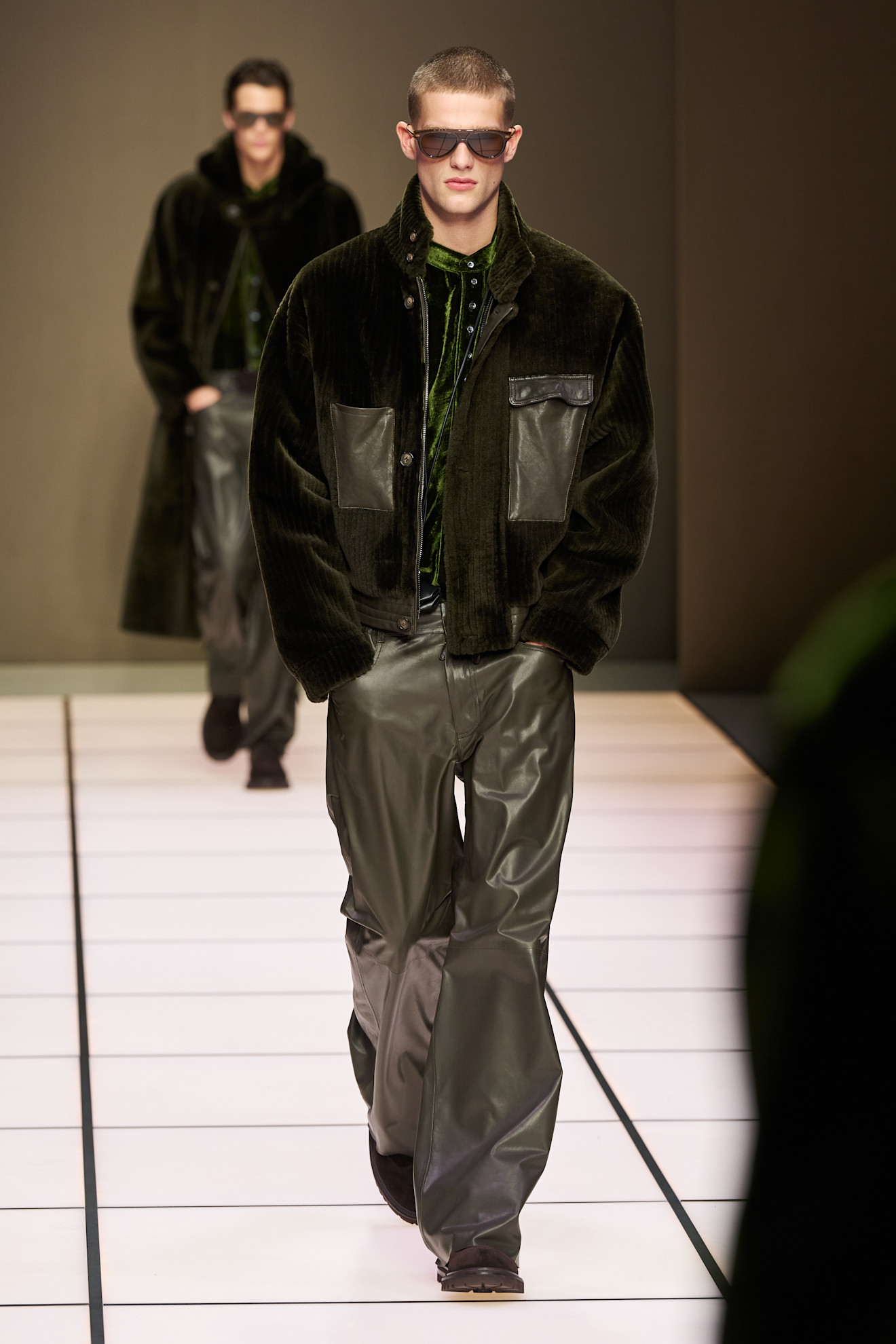 Модель в объемной куртке с кожаными вставками и широких брюках, завершает образ темными очками и уверенной походкой