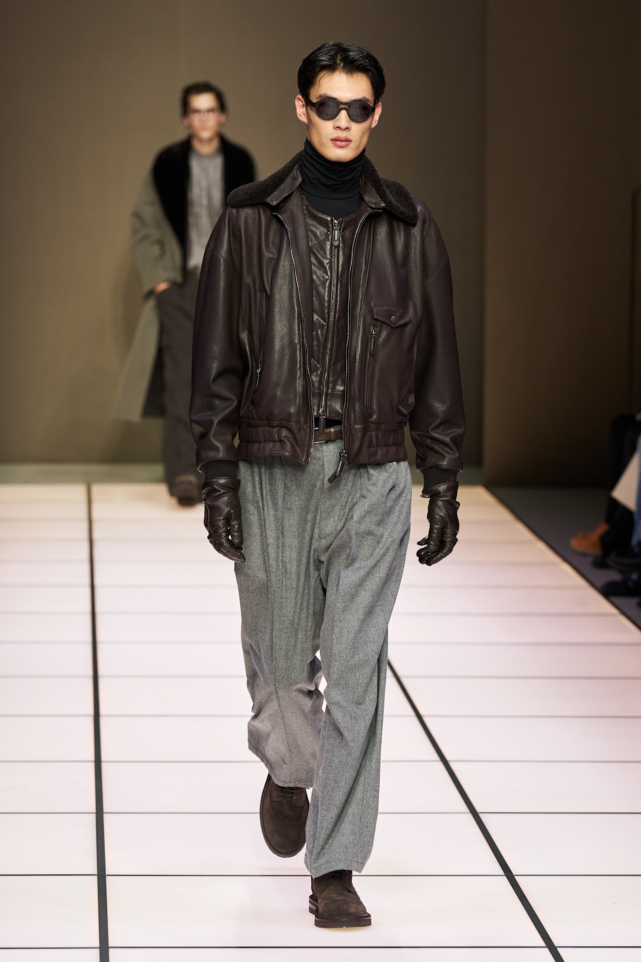 Модная кожаная куртка с меховым воротником, дополненная серыми брюками и темными очками, подчеркивающими уверенность модели