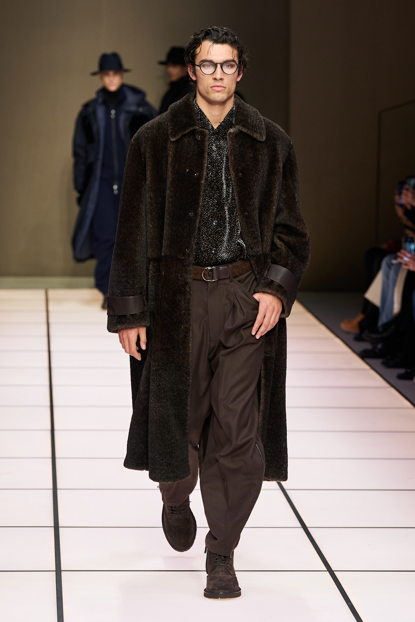 Модель в роскошном коричневом пальто с текстурированной отделкой, сочетает стиль с элегантным блестящим верхом