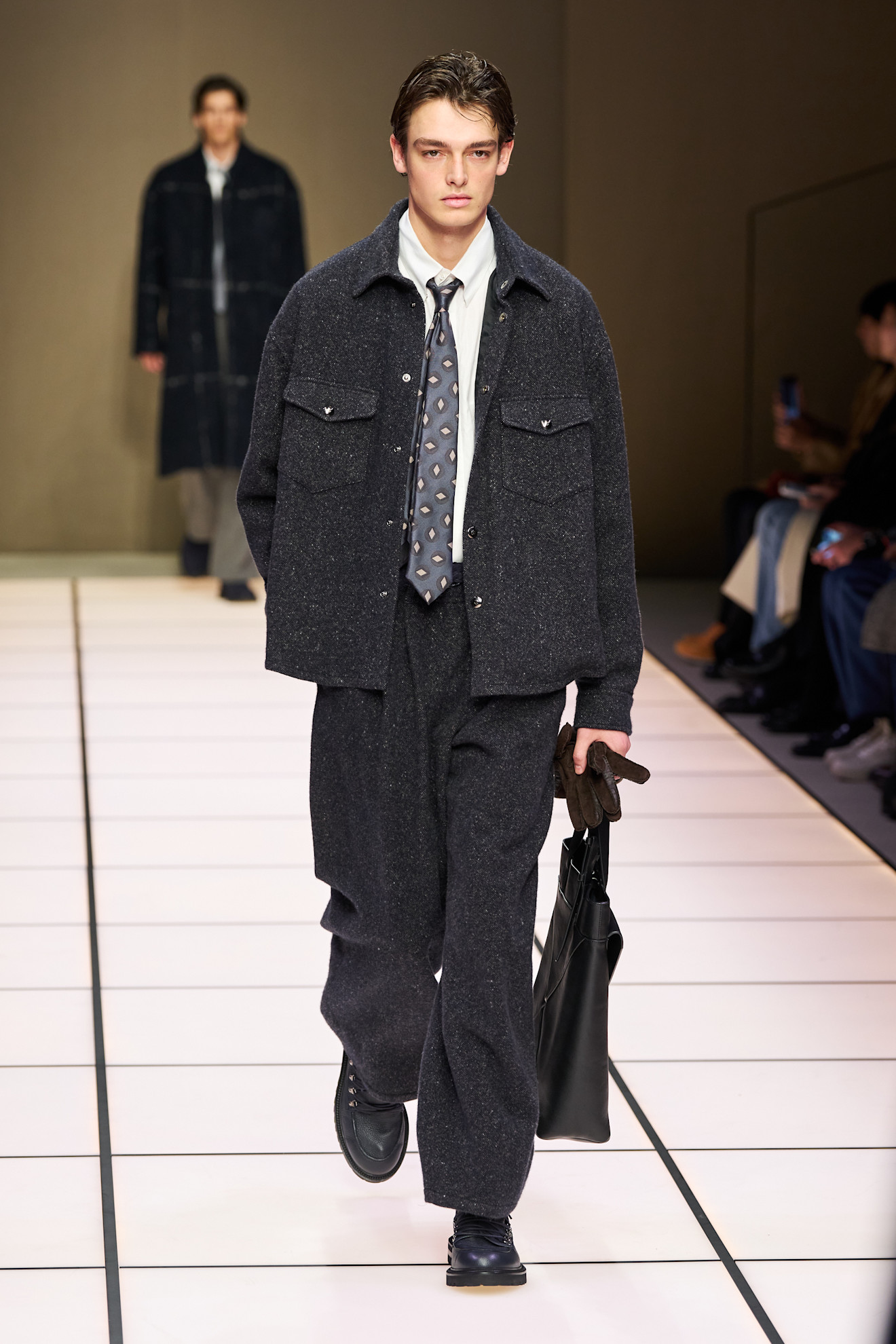 Модель в тёмно-сером шерстяном костюме с крупными карманами и галстуком, создающим элегантный контраст с обувью