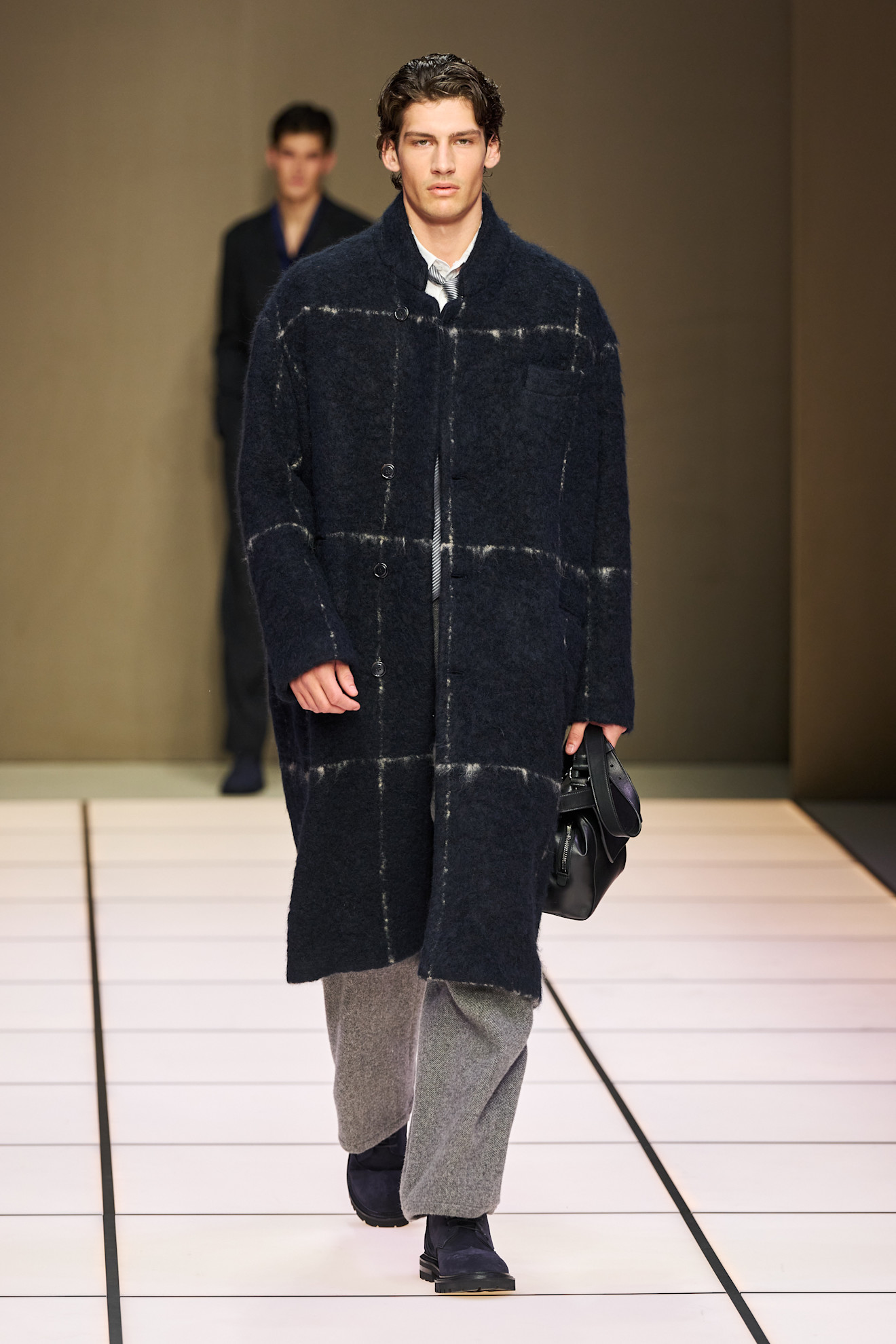 Мужчина в длинном тёплом пальто с клетчатым узором, сочетает его с серыми брюками и чёрной сумкой