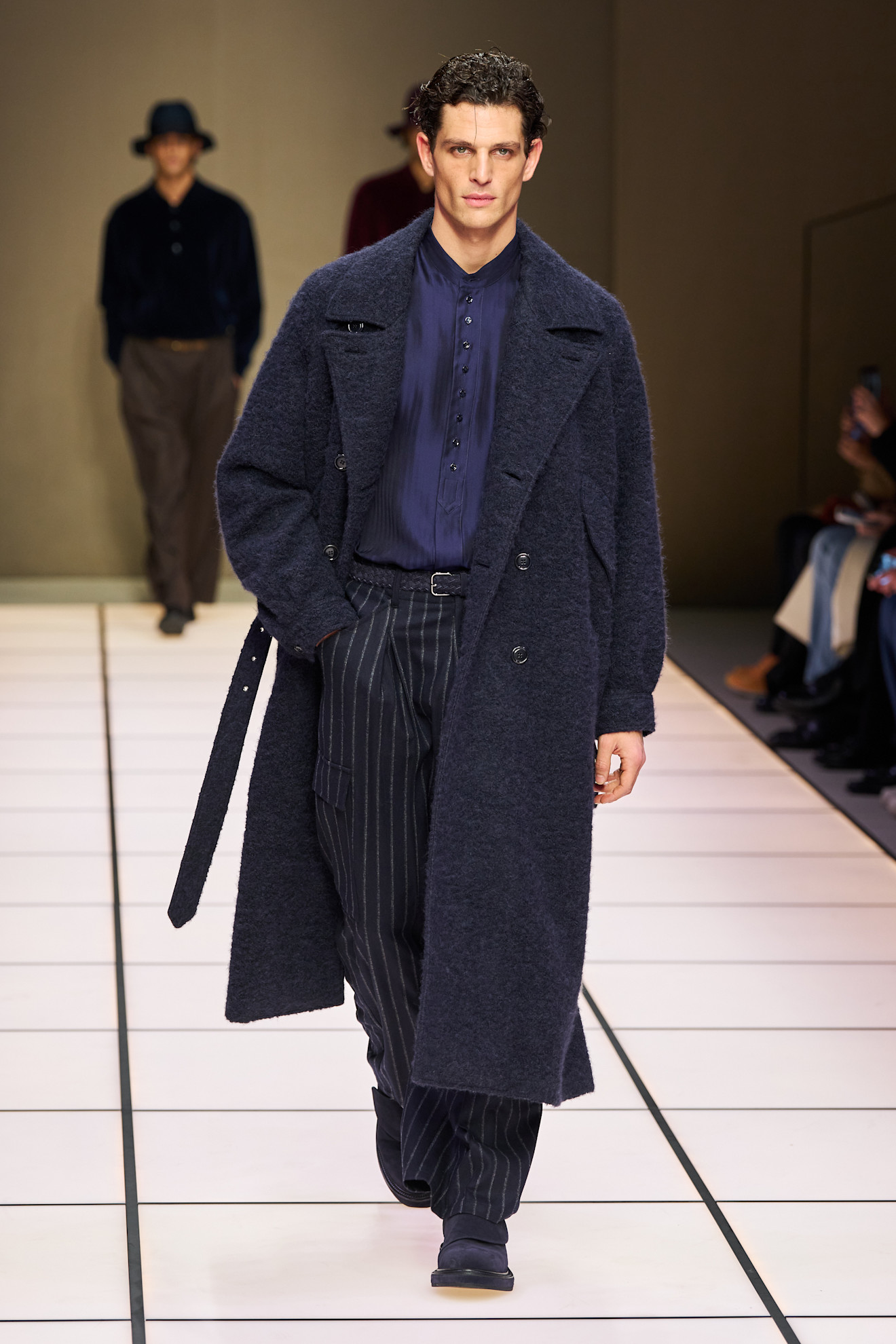 Модель в тёмно-синем пальто и полосатых брюках, дополняет образ элегантной рубашкой с пуговицами