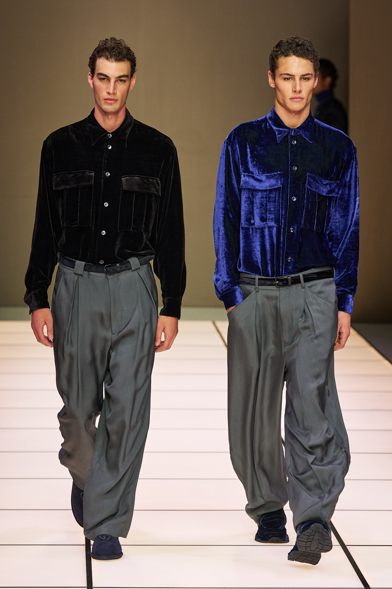 Два модели в бархатных рубашках, один черный и один синий, с широкими брюками, создают гармоничный дуэт на подиуме