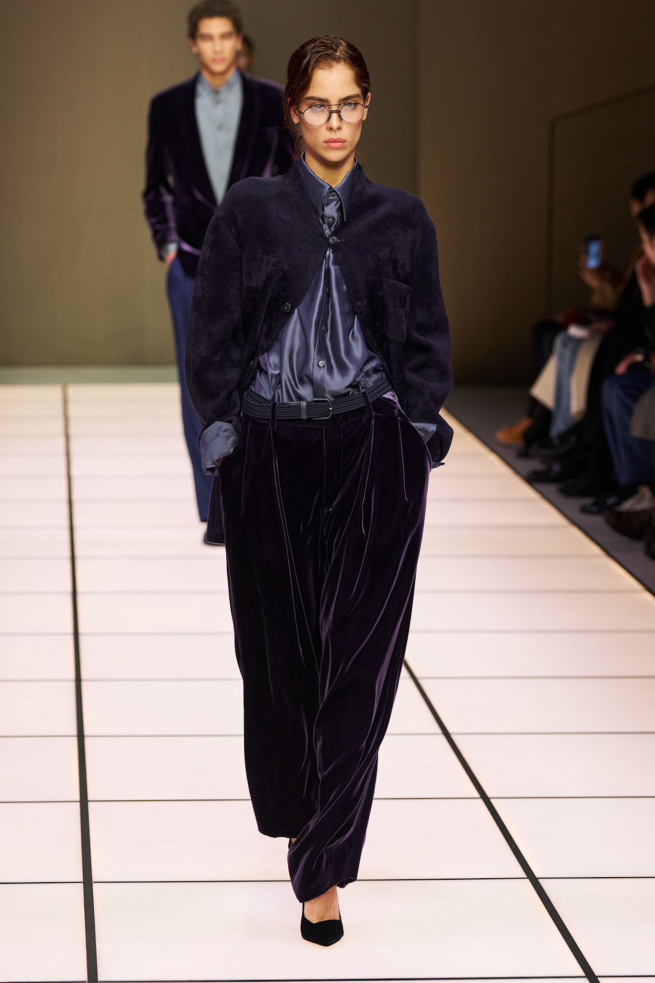 Женская модель в бархатном комплекте с пиджаком и брюками, дополненная очками, излучает уверенность и утонченность