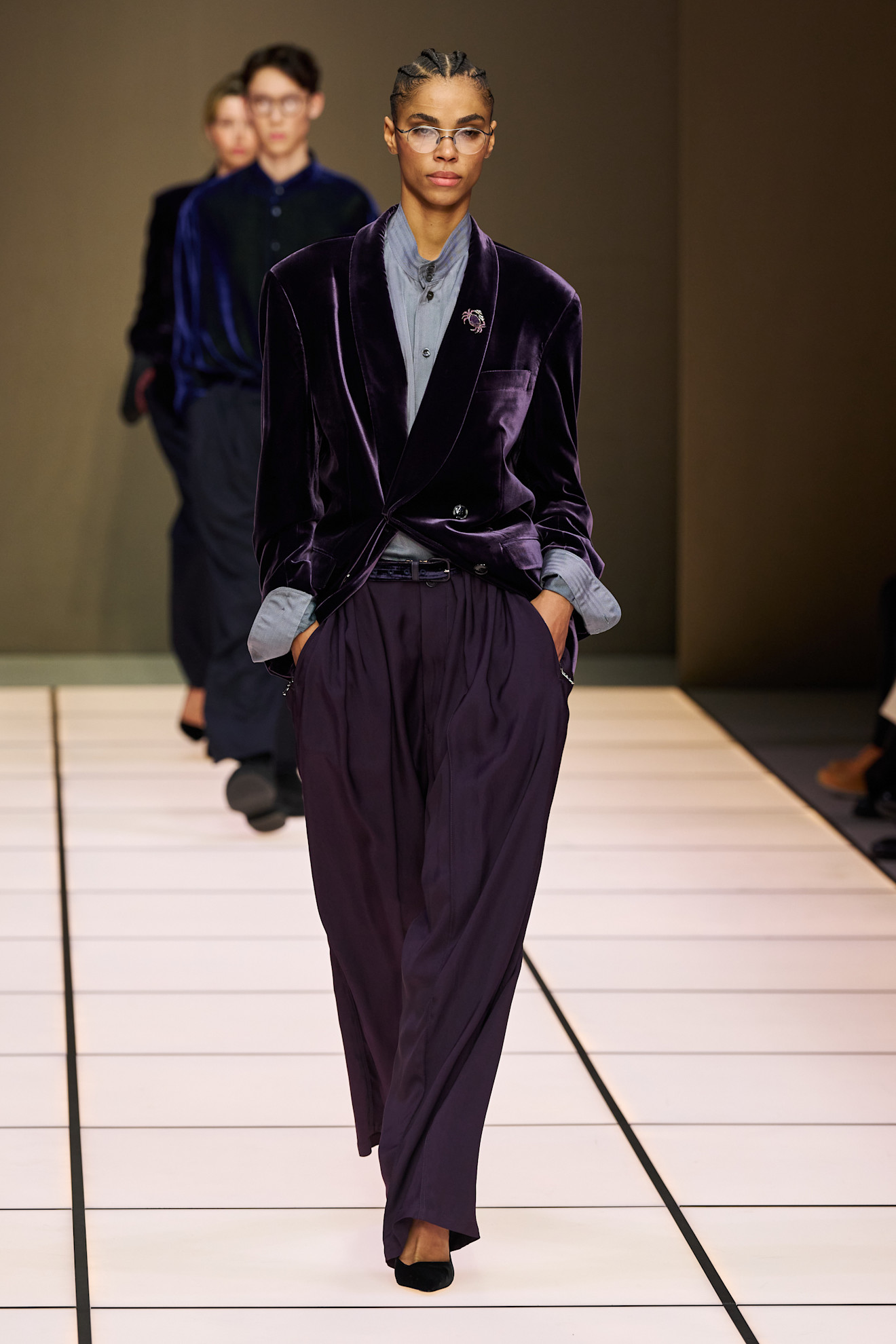 Модель с косичками в бархатном жакете и брюках, подчеркивающих силуэт, завершает образ стильной брошью на лацкане