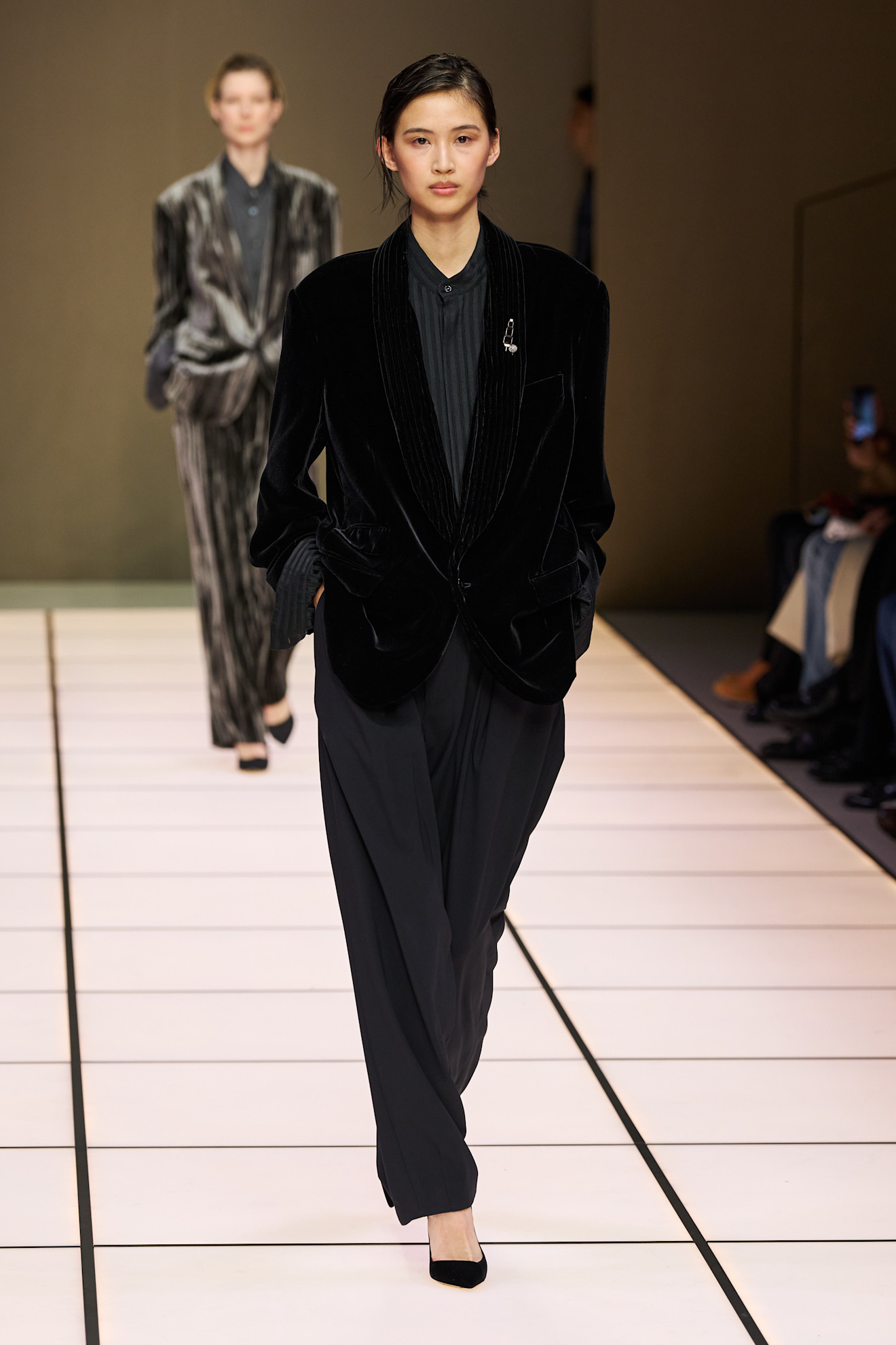 Модель в черном бархатном пиджаке и широких брюках, излучает элегантность и уверенность на подиуме