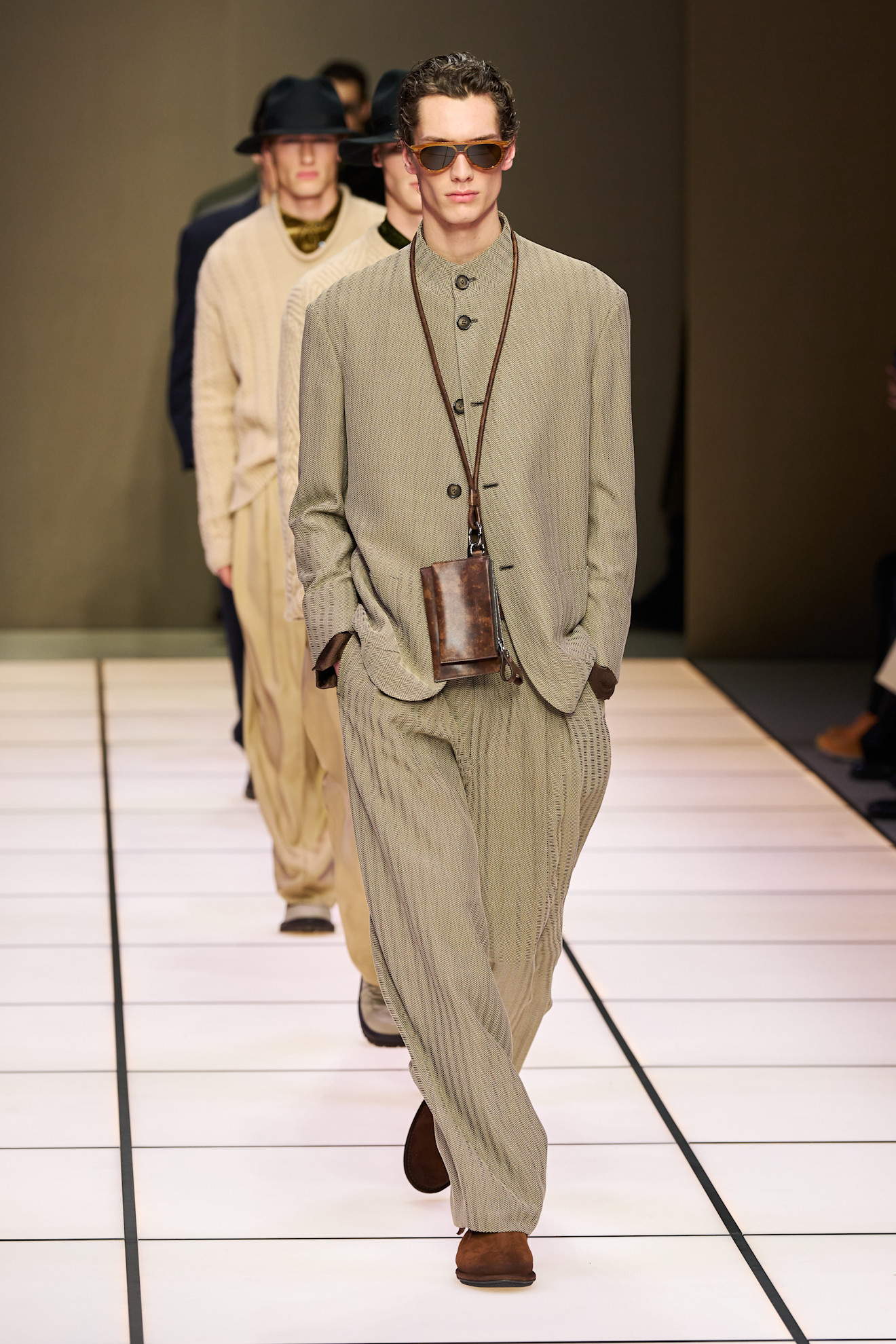 Модель в светлом костюме с текстурой в полоску, дополненном стильными очками и сумкой через плечо