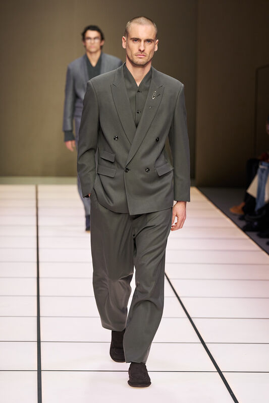 Строгий серый костюм с двойной застежкой, дополненный элегантной брошью, создает атмосферу уверенности и стиля