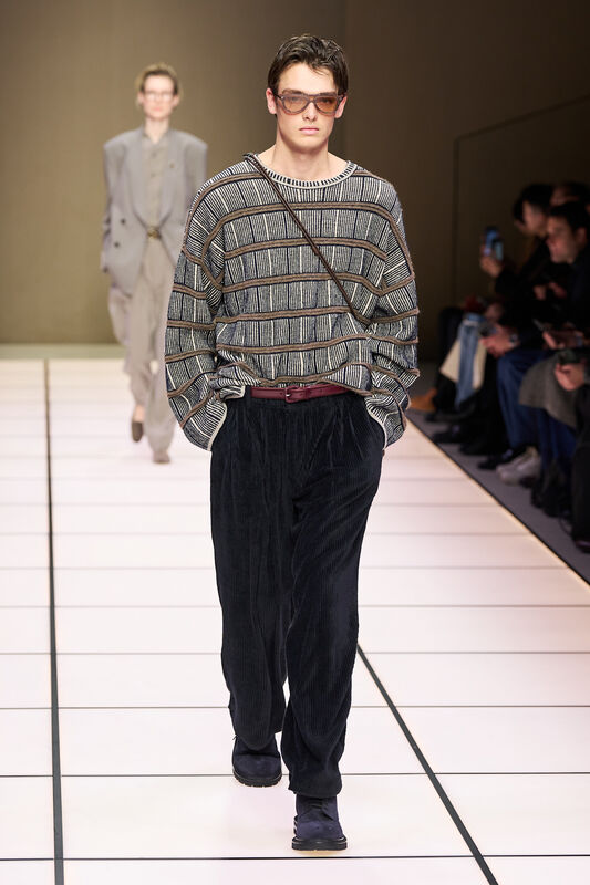 Модель в полосатом свитере и бархатных брюках, создающих уютный и современный вид, с акцентом на детали аксессуаров