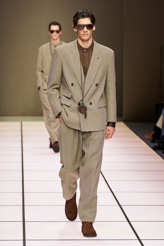 Модель в светлом двубортном костюме с текстурой и солнцезащитными очками, излучает уверенность и стиль