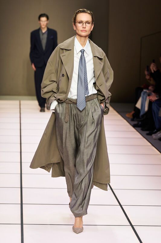 Женская модель в оливковом тренче и полосатом галстуке, сочетает строгость и стиль, уверенно демонстрируя образ