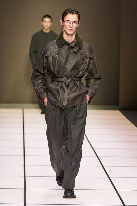 Мужчина в кожаном пиджаке с меховым воротником и широких брюках, излучает уверенность и стильный шик на подиуме