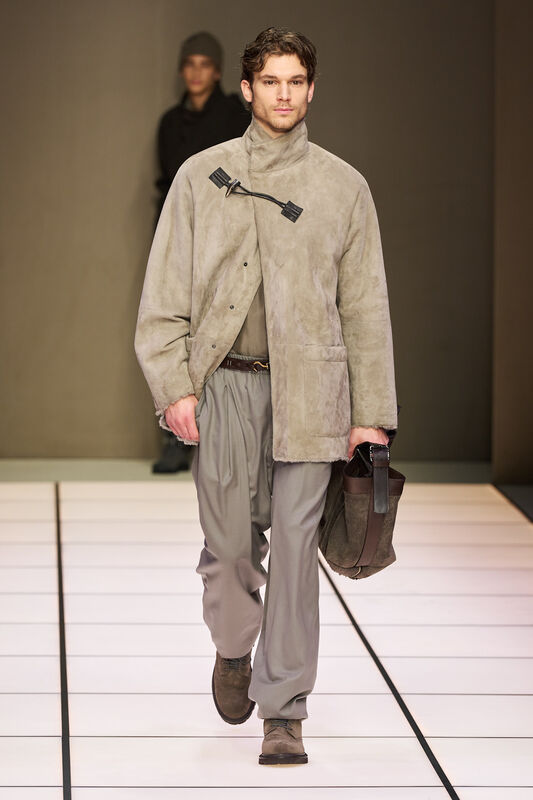 Модель в замшевой куртке с высоким воротником и свободных брюках, дополняет образ стильной сумкой