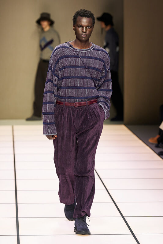 Манекенщик в полосатом свитере и велюровых брюках, с поясом в тон, демонстрирует расслабленный стиль в осенней коллекции