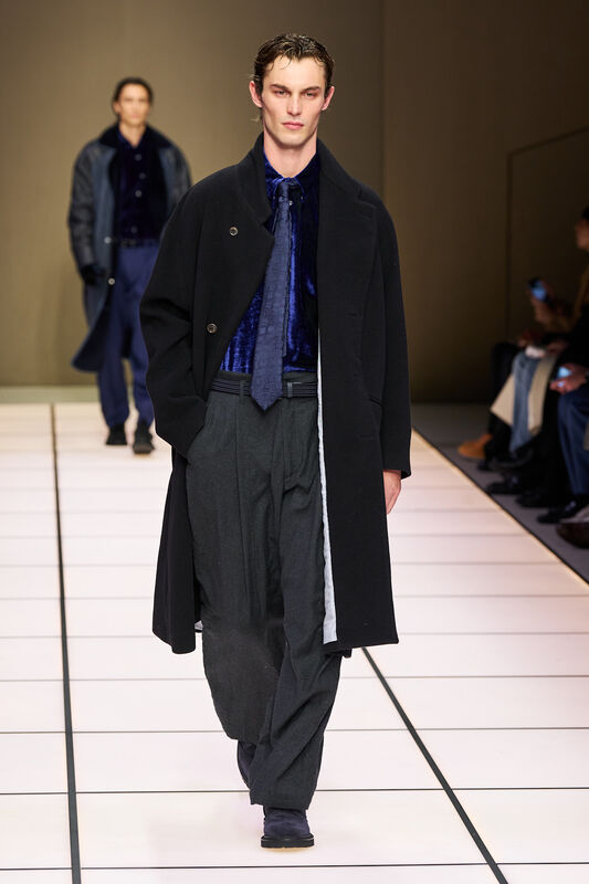 Элегантный черный плащ с глубоким воротником, бархатная рубашка и широкие брюки в сером оттенке создают стильный образ