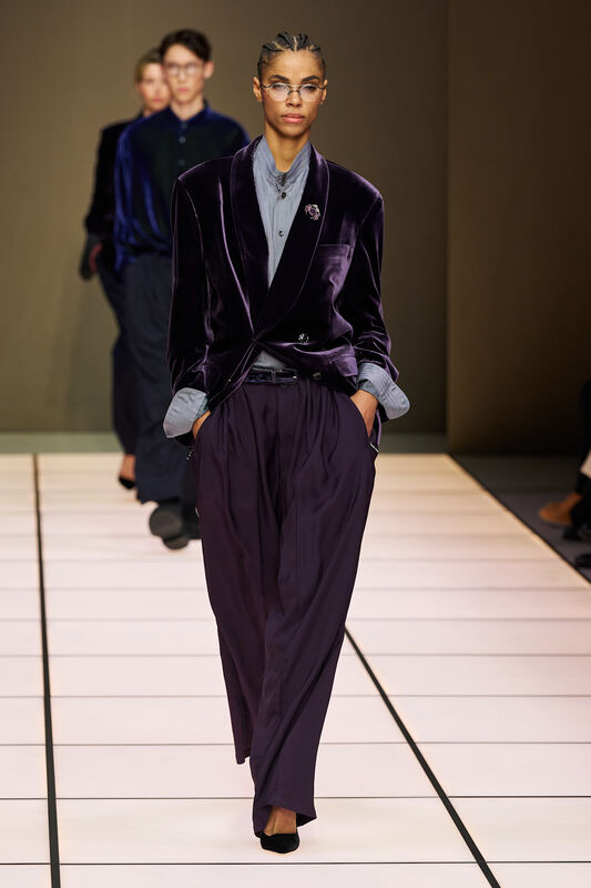 Модель с косичками в бархатном жакете и брюках, подчеркивающих силуэт, завершает образ стильной брошью на лацкане