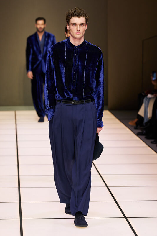 Мужчина в бархатной рубашке с пуговицами и свободных брюках, демонстрирует уверенность и современность