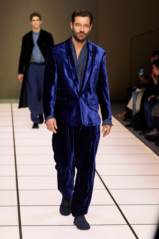 Мужчина в ярком бархатном костюме с принтом, уверенно идет по подиуму, создавая эффектный образ для осени-зимы