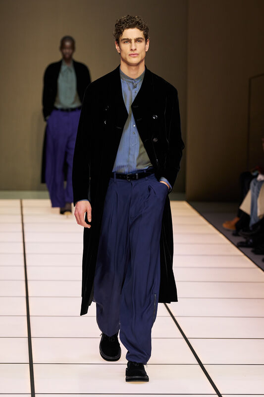 Элегантный образ с черным бархатным пальто и широкими синими брюками, подчеркивающий уверенность модели