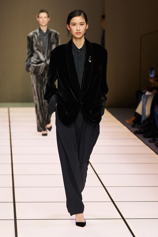 Модель в черном бархатном пиджаке и широких брюках, излучает элегантность и уверенность на подиуме