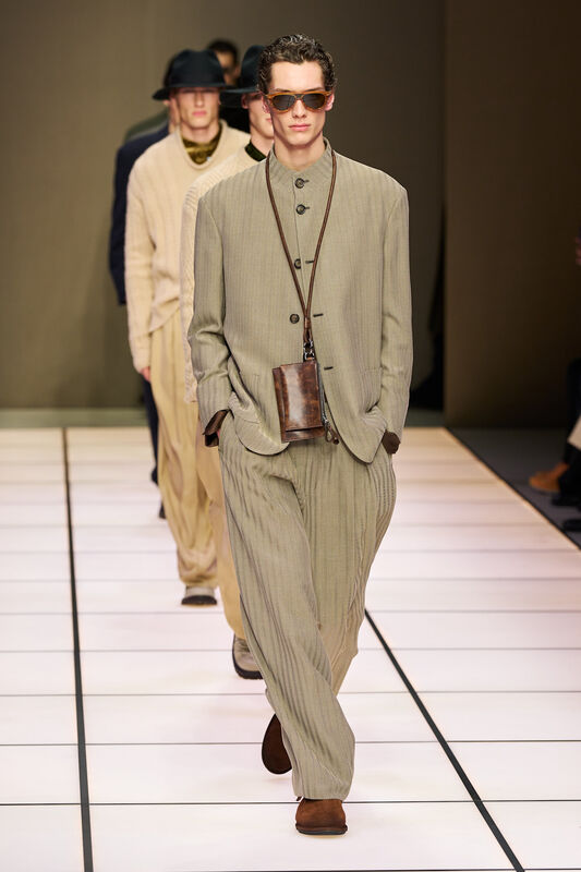 Модель в светлом костюме с текстурой в полоску, дополненном стильными очками и сумкой через плечо