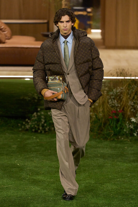 Модель в тёплом пуховике с логотипом и строгом костюме, держит яркую сумку, создавая контраст между стилями и текстурами