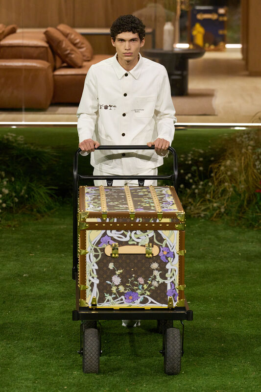 Модель с тележкой, на которой стоит яркий чемодан с цветочным принтом, подчеркивает уникальность коллекции