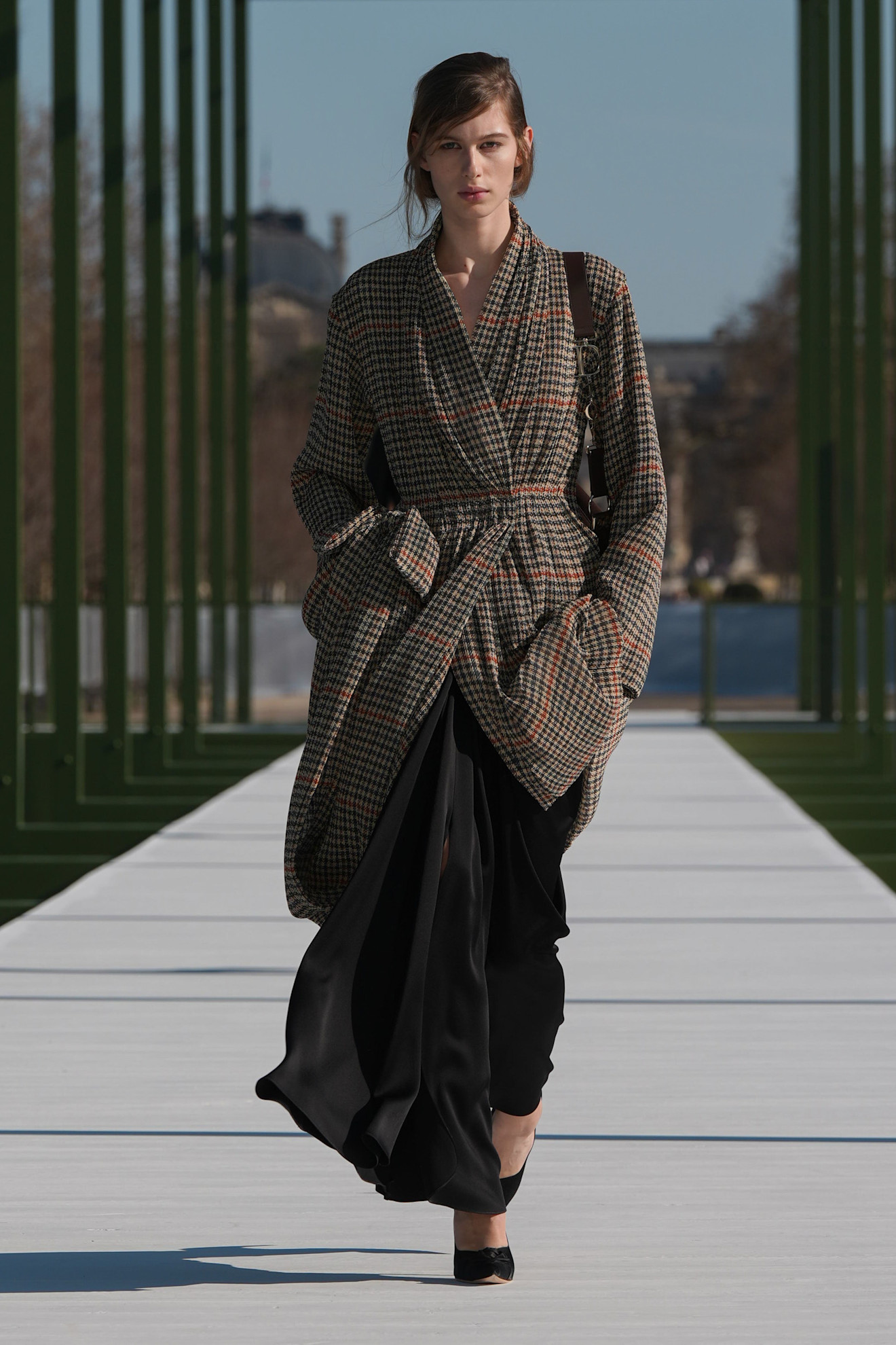 Платье с крупным клетчатым узором, свободный силуэт и черные брюки создают стильный контраст на фоне ясного неба
