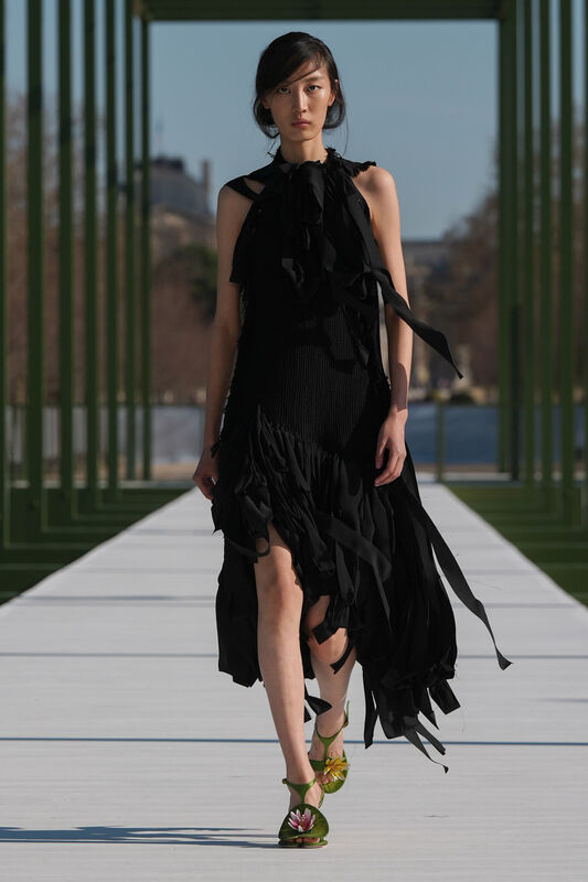 Модель в черном платье с рваными элементами и открытыми плечами, яркие туфли с цветами подчеркивают стиль