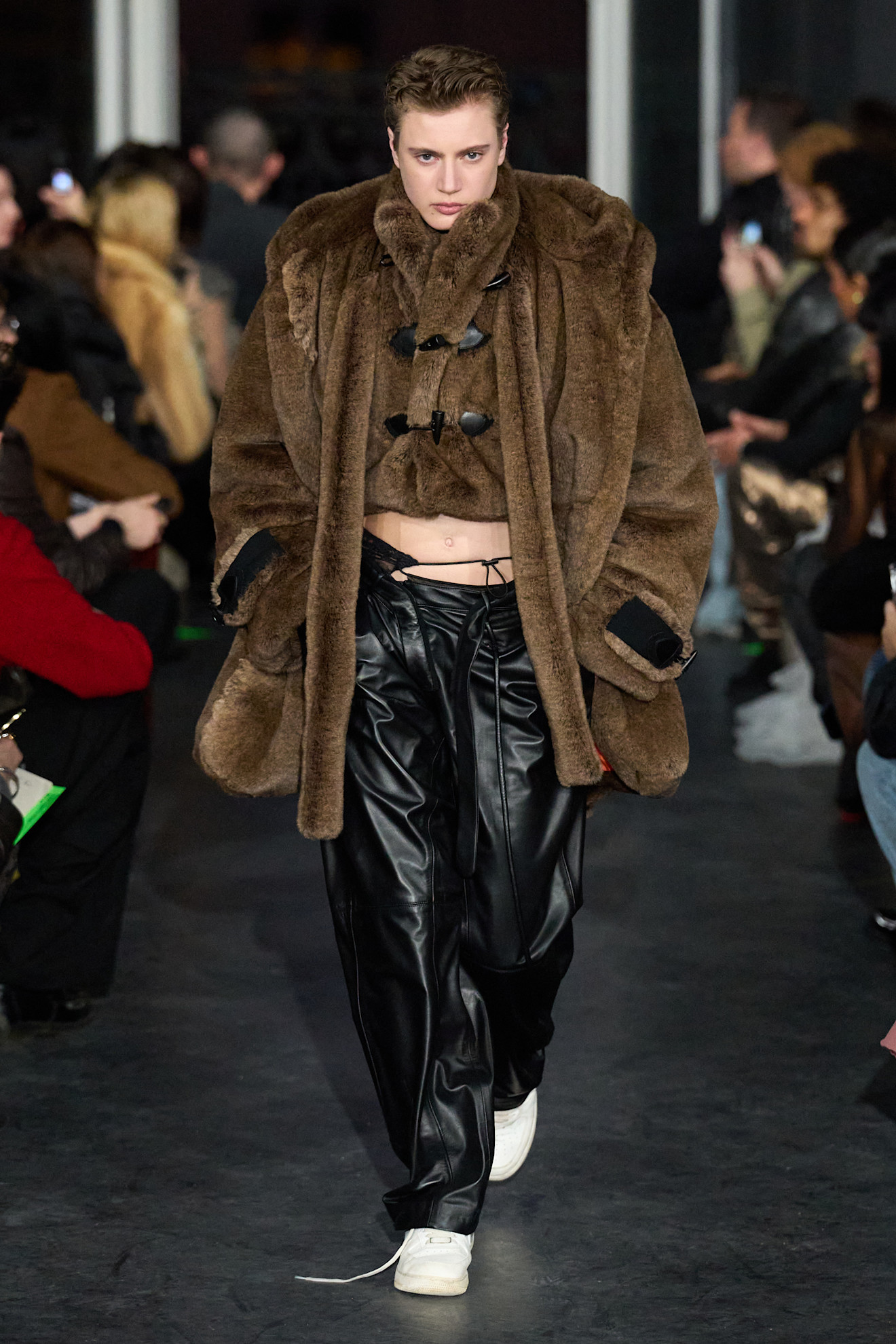 Объемный коричневый меховой пиджак с закругленным воротником и черными кожаными брюками, создающими контрастный образ