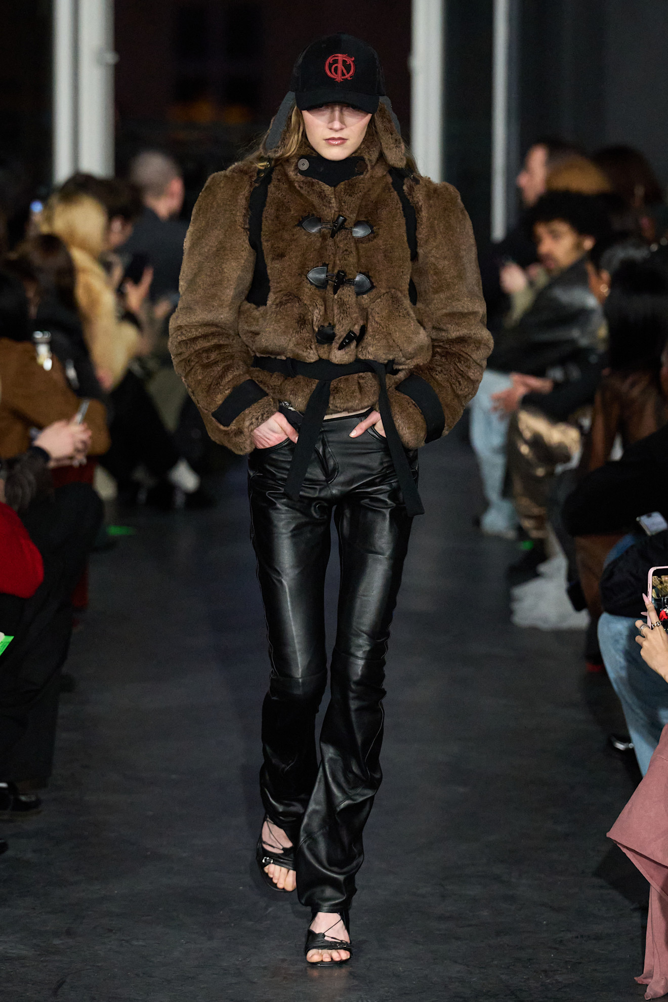 Модель в меховом жакете с капюшоном и черной бейсболкой, сочетает стиль с элегантностью в черных кожаных брюках