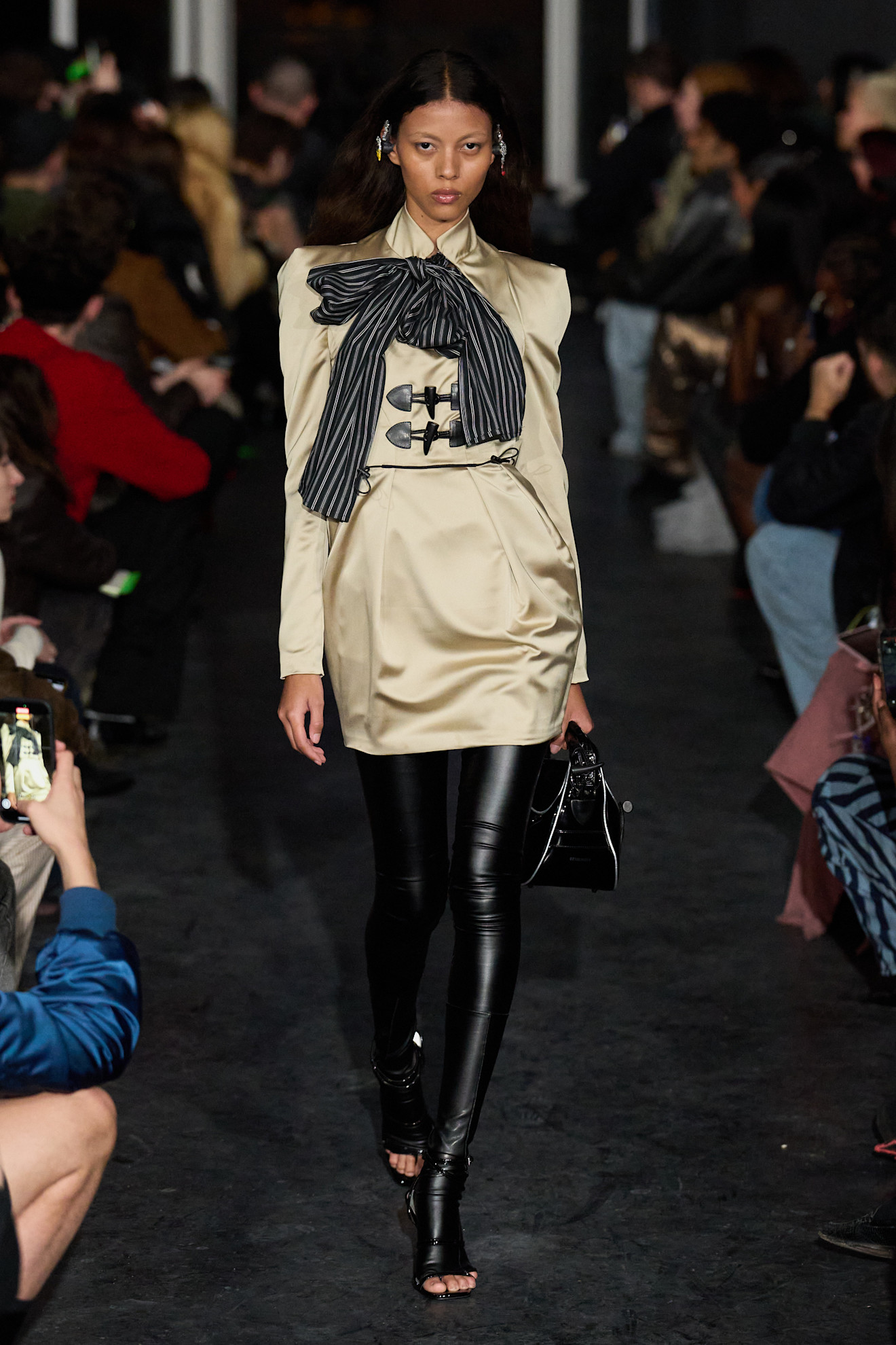 Девушка в светлом платье с крупным бантом и черными леггинсами, сочетает классические и современные элементы, привлекая внимание на подиуме