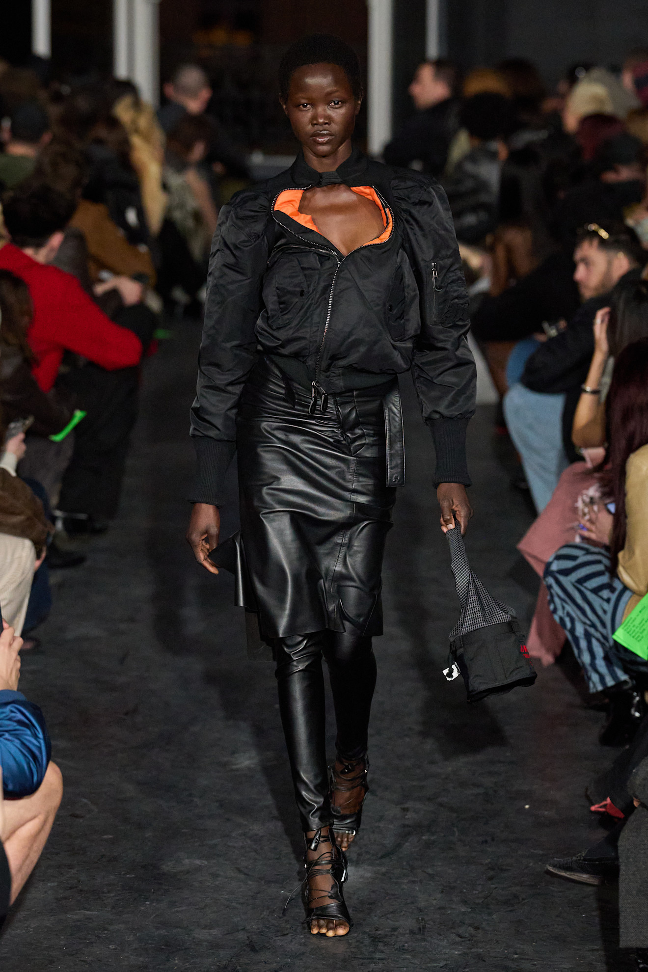 Образ с бомбером и кожаной юбкой, яркий акцент на оранжевом топе, подчеркивает смелость и индивидуальность модели