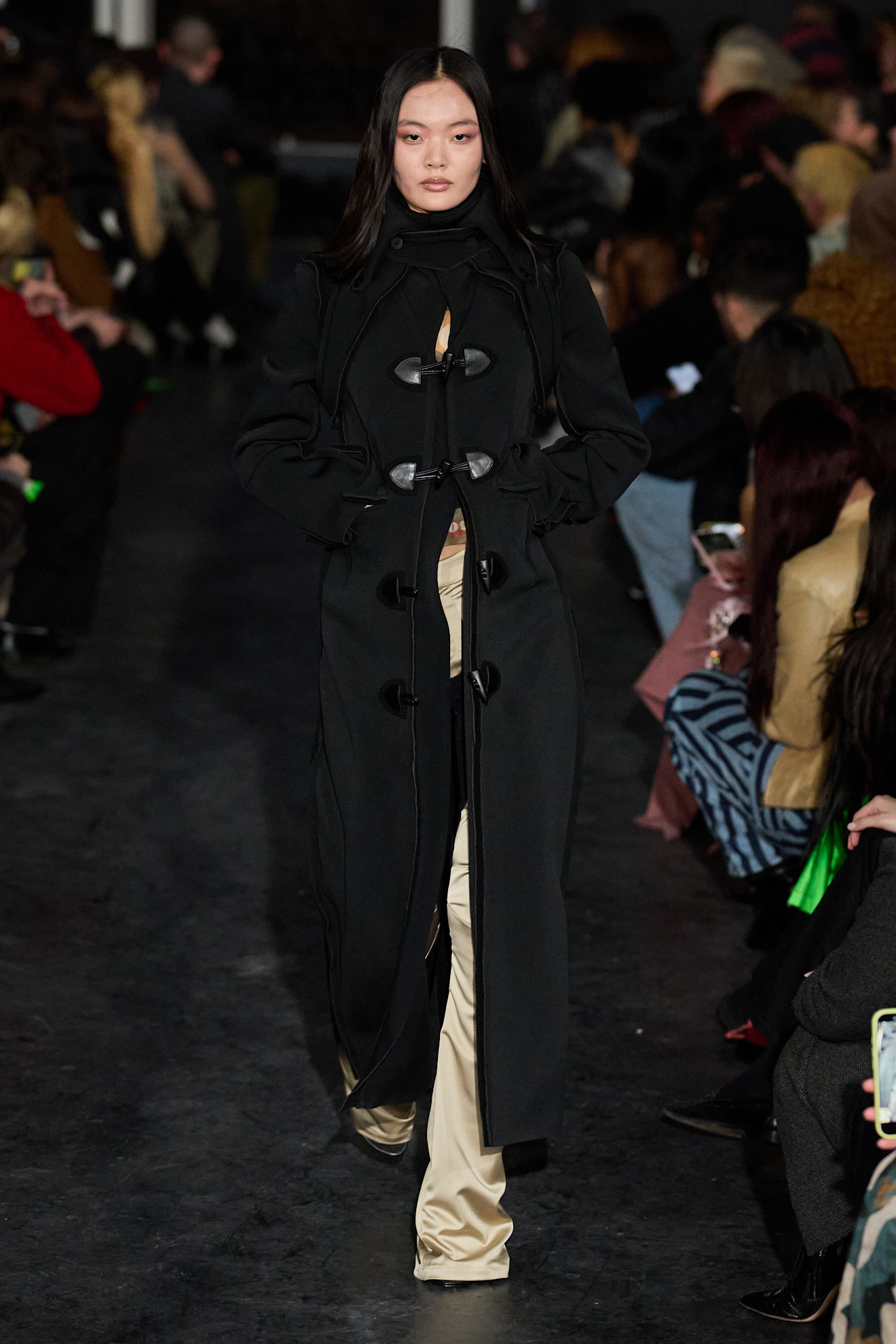 Элегантное черное пальто с необычными застежками, под ним виднеются светлые брюки, создающие контраст