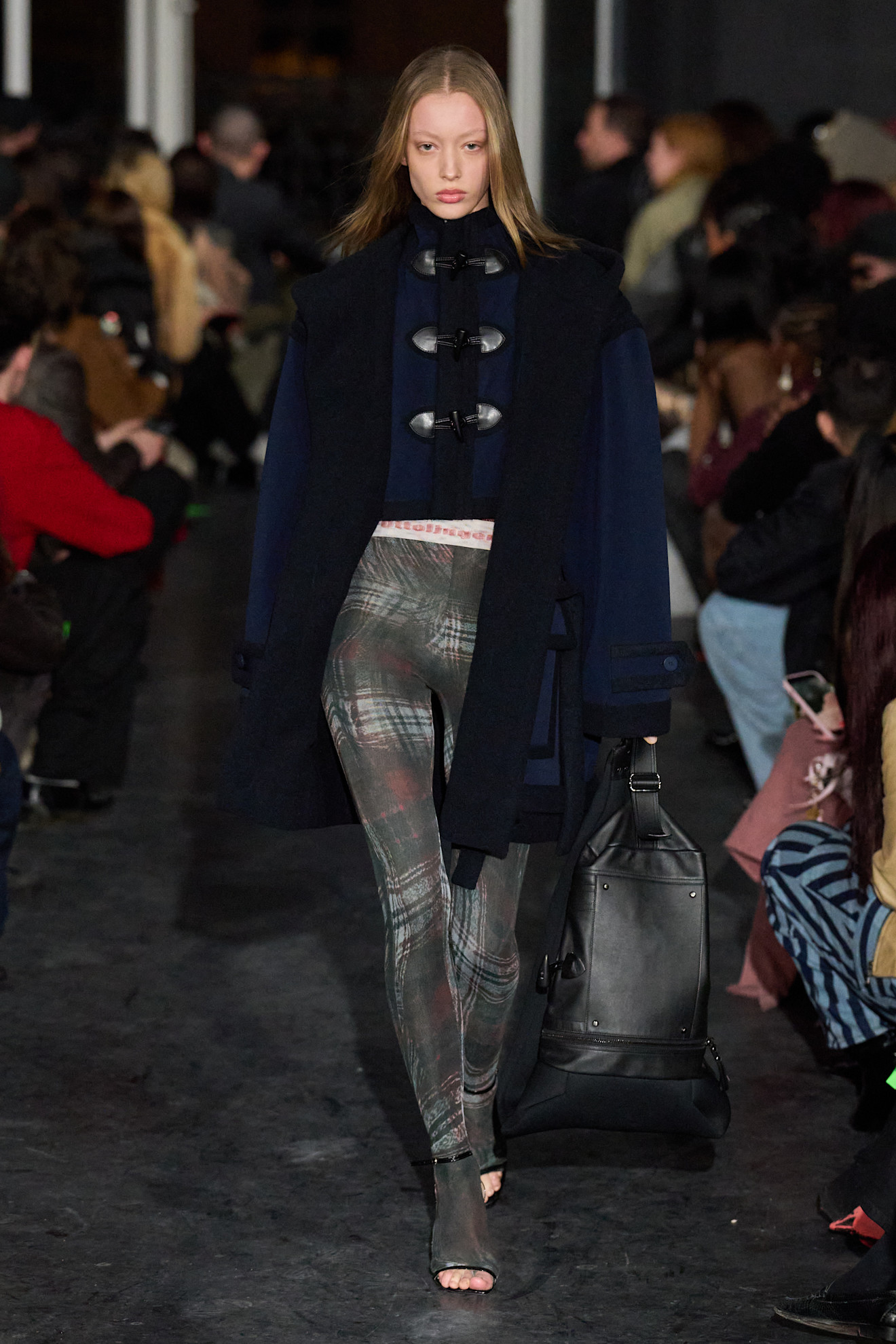 Модель в тёмно-синем пальто с характерными застёжками и облегающих леггинсах в клетку, создающих стильный контраст