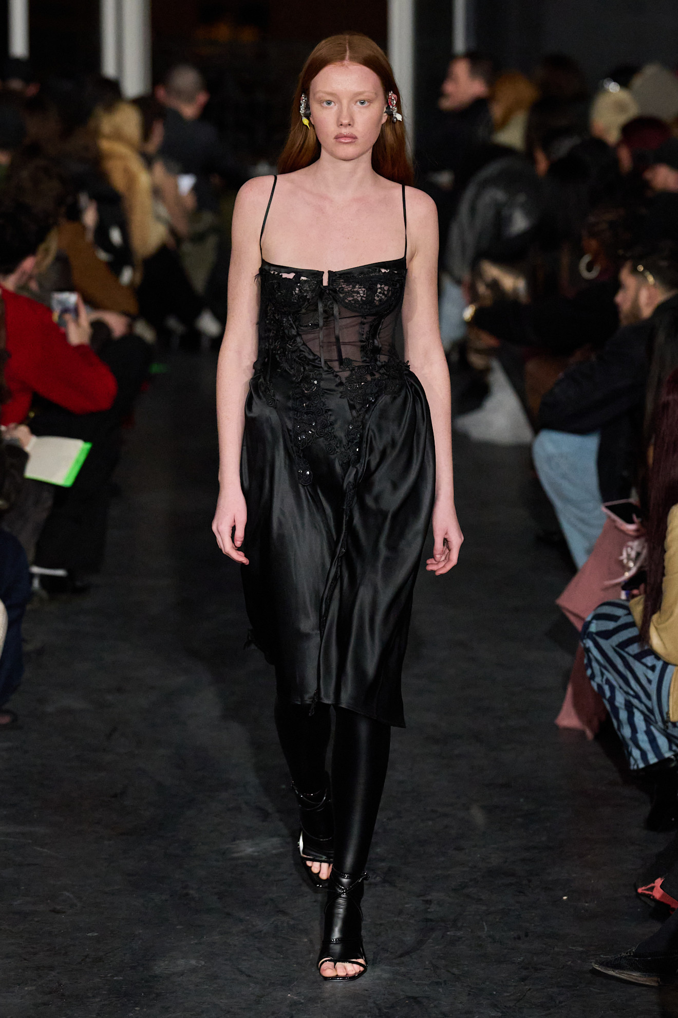 Прозрачное черное платье с вышивкой, обрамляющее фигуру, создает загадочный образ на фоне зрителей