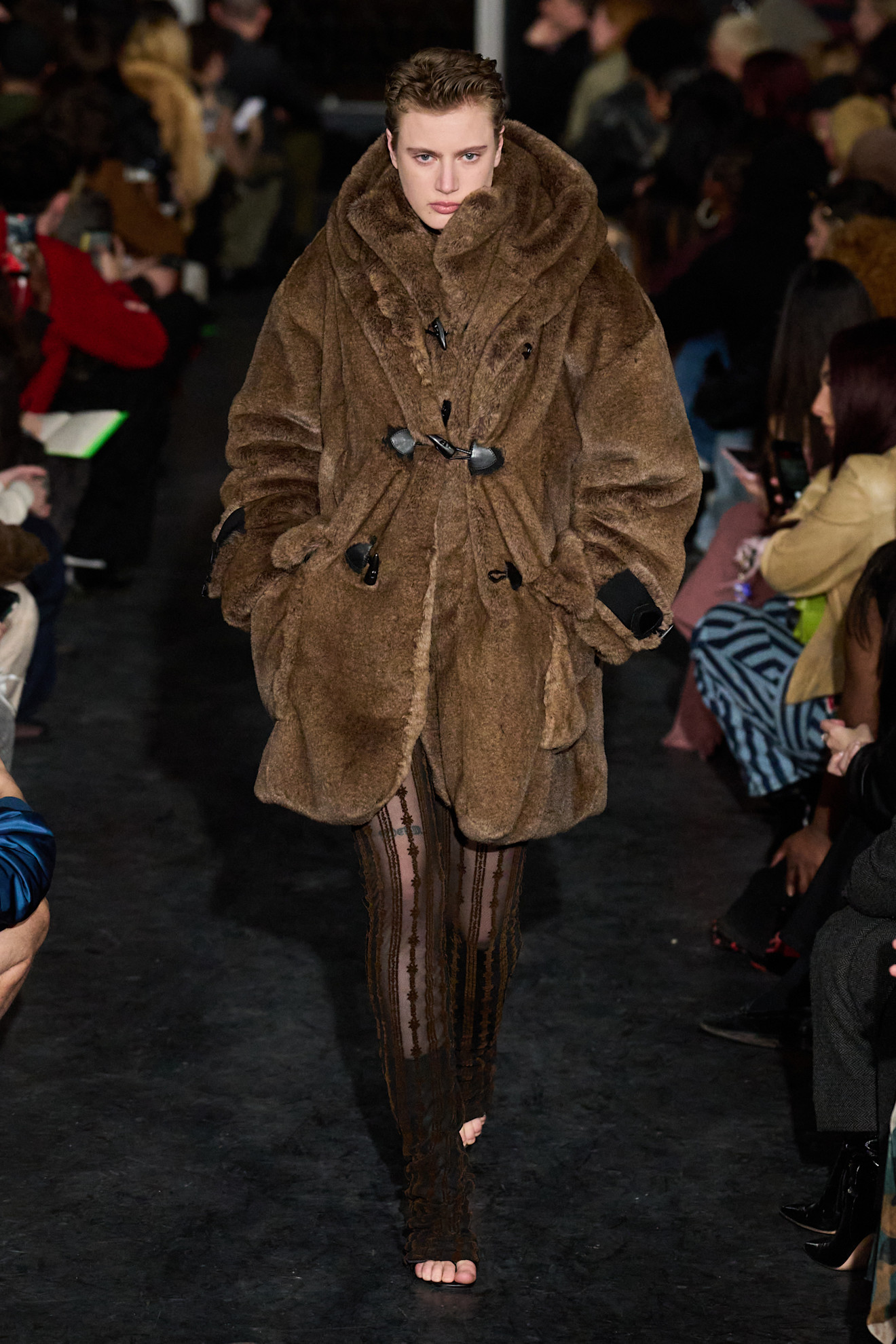 Уютный коричневый меховой плащ с крупным воротником, гармонирующий с облегающими прозрачными брюками