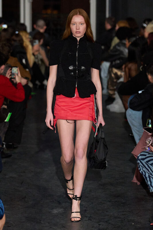 Модель в черном жакете с объемными рукавами и короткой красной юбке, акцент на контрасте текстур и силуэтов