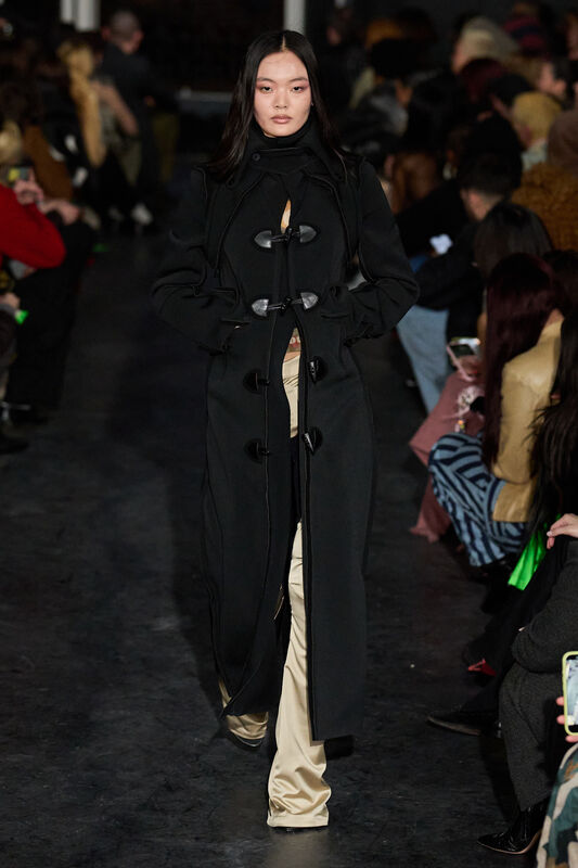 Элегантное черное пальто с необычными застежками, под ним виднеются светлые брюки, создающие контраст